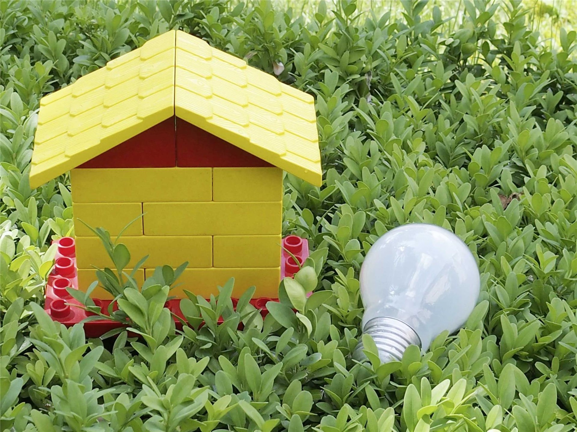 gelbes Haus aus Lego im Gras, daneben eine Glühlampe