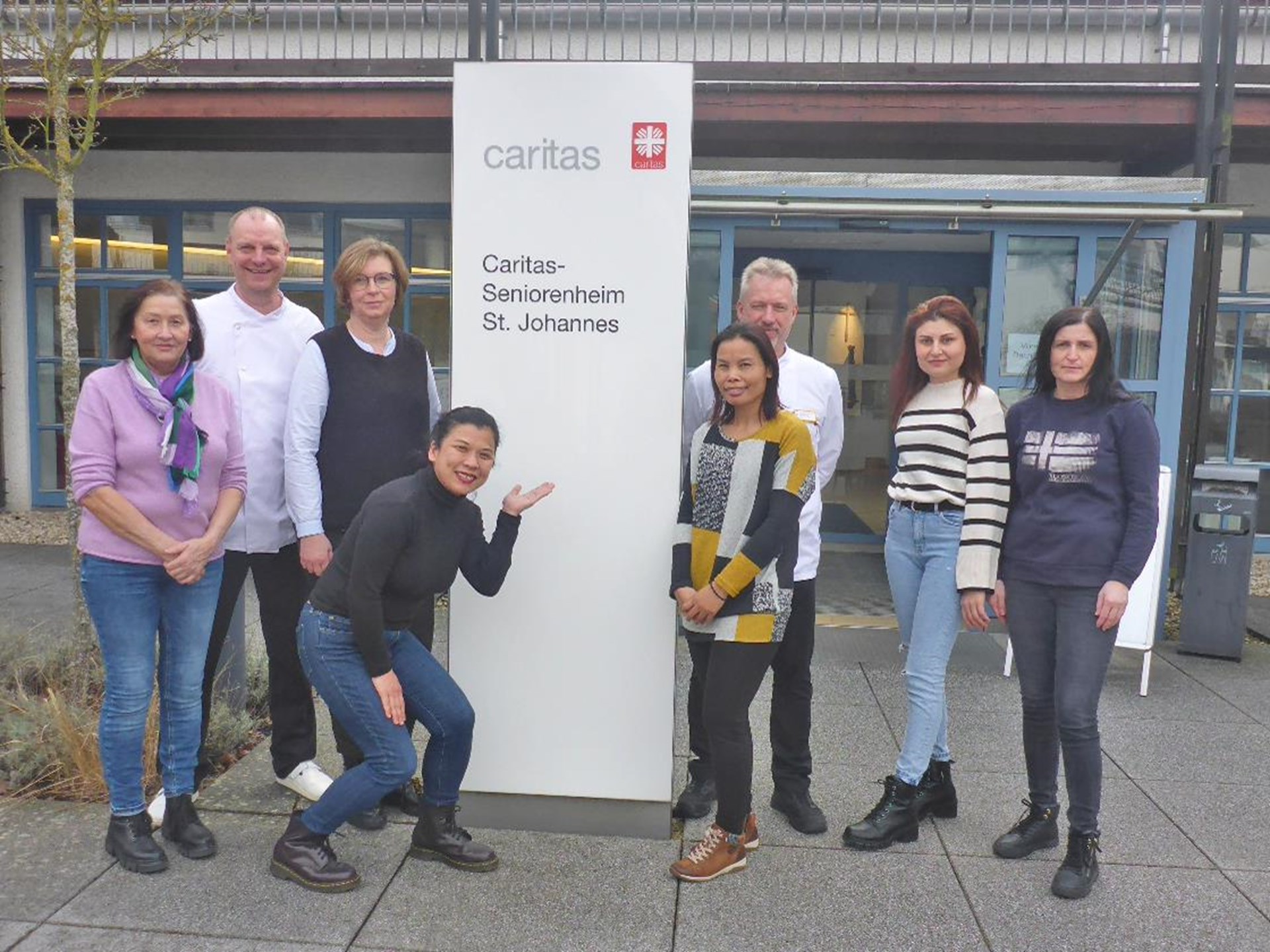 Küchenteam: Acht Männer und Frauen stehen um Caritasstele herum