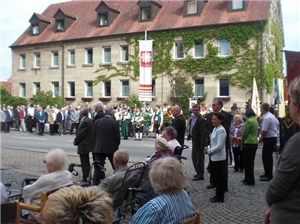 Viele Menschen und eine Musikkapelle stehen im Halbkreis vor dem Altenheim. Senioren sitzen auf Rollstühlen oder Stühlen dabei.