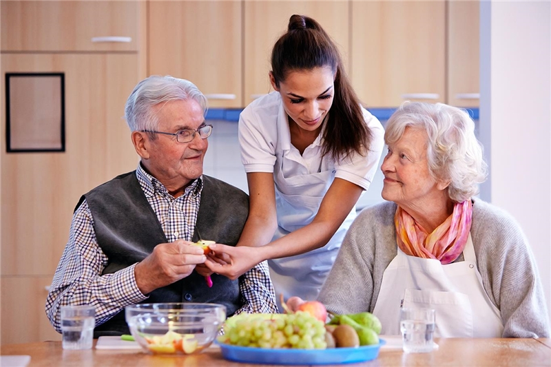 Zwei ältere Menschen bekommen Essen gereicht von einer jungen Frau.